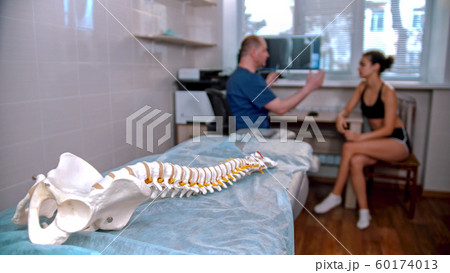 Chiropractic treatment - the doctor inspecting the young woman before the session - model of the human spine placed on the couch in the cabinet Chiropractic treatment - the doctor inspecting the young woman before the session - model of the human spine placed on the couch in the cabinet 60174013