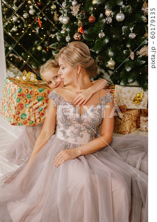 Daughter hugging her mother while sitting at christmas tree with gift boxes 60179135