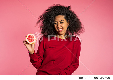 African american girl act ape her face from grapefruit cid. Woman grimaces. Lady with curly hairstyle on pink background. Diet. healthy lifestyle concept. African american girl act ape her face from grapefruit cid. Woman grimaces. Lady with curly hairstyle on pink background. Diet. healthy lifestyle concept. 60185756
