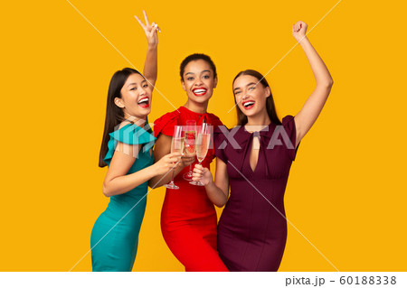 Three Models Clinking Glasses Having Fun Standing Over Yellow Background 60188338