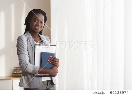 Young black secretary standing with clipboard and notebook in office Young black secretary standing with clipboard and notebook in office 60188974