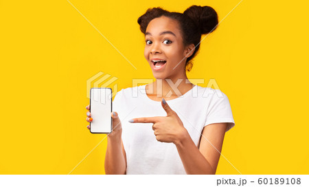 Amazed black girl pointing at blank white mobile screen Amazed black girl pointing at blank white mobile screen 60189108