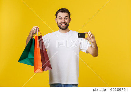 portrait of smiling couple holding shopping bags and credit card isolated on yellow background. 60189764