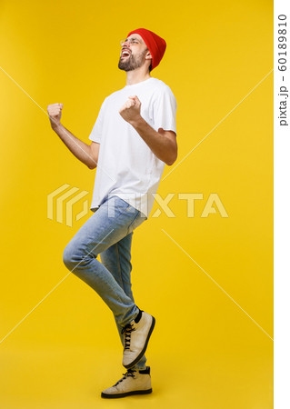 Happy young man with arms up isolated on a yellow background. 60189810