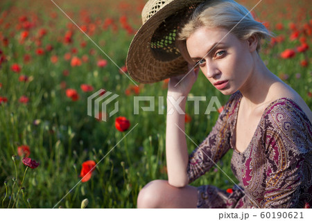 Beautiful fashionable blonde woman in a hat in a field of red flowers Beautiful fashionable blonde woman in a hat in a field of red flowers 60190621