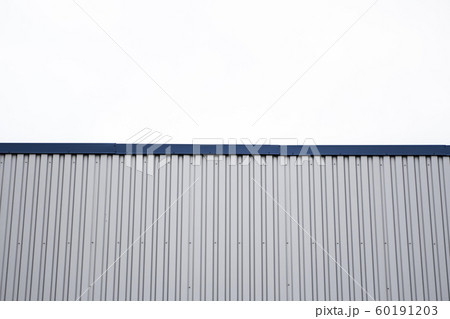 Metal corrugated sheets on a building with a blue metal corners. White aluminium metal corrugated roof or wall sheets against cloudy sky background on a factories and industrial buildings. 60191203