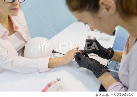 Top view, woman manicurist doing manicure, painting nails, using ultraviolet lamp for fixing gel nail polish. Nail and hand care in beauty salon Top view, woman manicurist doing manicure, painting nails, using ultraviolet lamp for fixing gel nail polish. Nail and hand care in beauty salon 60193916