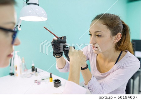 Woman in nail salon receiving manicure by manicurist, closeup manicure process. Nail and hand care in beauty salon. 60194007