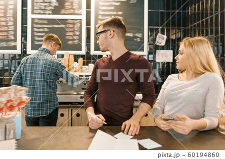 Young people working in coffee shop, man and woman near bar counter, receiving order by phone, barista on the background of coffee machine. Teamwork, staff, small business, people concept Young people working in coffee shop, man and woman near bar counter, receiving order by phone, barista on the background of coffee machine. Teamwork, staff, small business, people concept 60194860