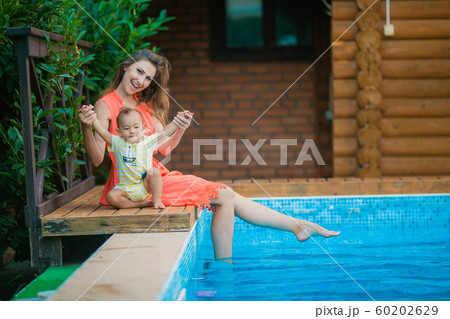 Mom with young son on the edge of the pool sitting on a chair for sun treatments 60202629