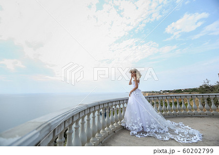 A bride in a beautiful white wedding dress stands on a balcony at the top of a mountain on a Sunny 60202799