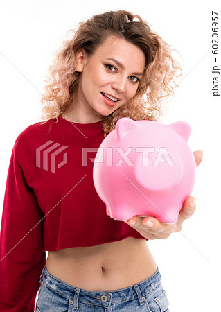 European attractive girl holds a piggy bank in hands on a white studio wall, 60206957