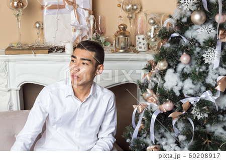 Young man sitting on couch near christmas tree and Young man sitting on couch near christmas tree and 60208917