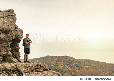 Young man with a backpack on top of cliff enjoying 60209508