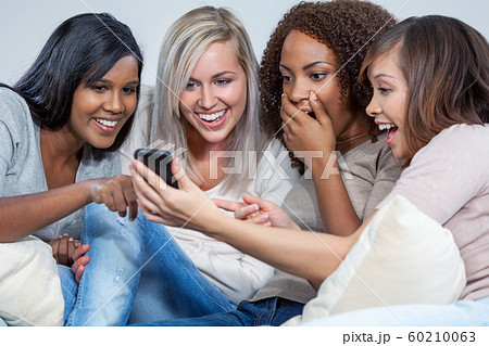 Interracial Group of Female Friends Laughing at Social Media on a Mobile Cell Phone Interracial Group of Female Friends Laughing at Social Media on a Mobile Cell Phone 60210063