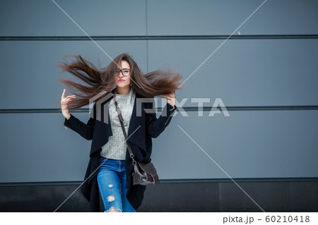 Woman model on the street in a gray coat with long dark hair against a solid wall 60210418