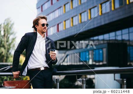 A Man With A Nice Beard Is Standing In The Street In A Blue Suit And An Orange Leather Bag While Drinking His Coffee A Man With A Nice Beard Is Standing In The Street In A Blue Suit And An Orange Leather Bag While Drinking His Coffee 60211448