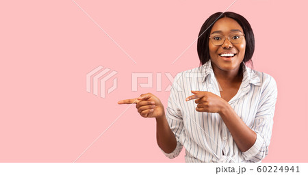 Smiling Afro Woman Pointing Fingers Aside Standing Over Pink Background 60224941