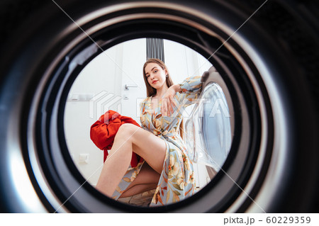 Young woman at home puts the dress in the drying machine. Young woman at home puts the dress in the drying machine. 60229359