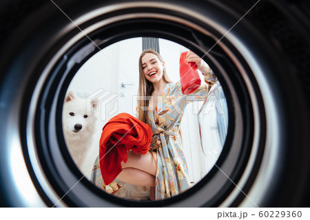 Young woman at home puts the dress in the drying machine. Young woman at home puts the dress in the drying machine. 60229360