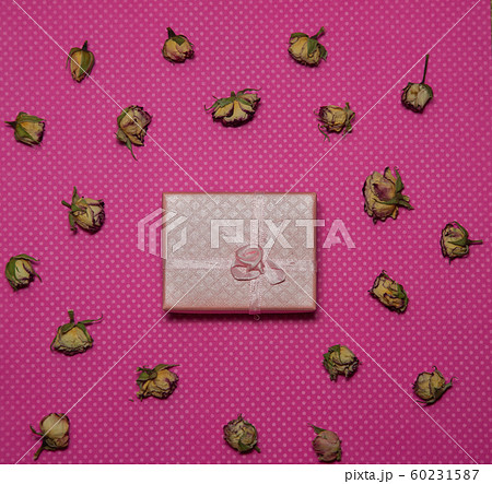 Photo flat lay gift box with bow among dried rose buds on a pink background top view 60231587
