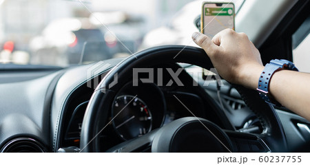 Close up of a man's hand holding the steering wheel of a car By using a smartphone Close up of a man's hand holding the steering wheel of a car By using a smartphone 60237755