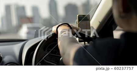 Close up of a man's hand holding the steering wheel of a car By using a smartphone 60237757
