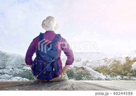 Rear view of an Asian man in a hat with a backpack sitting on the wooden floor 60244599