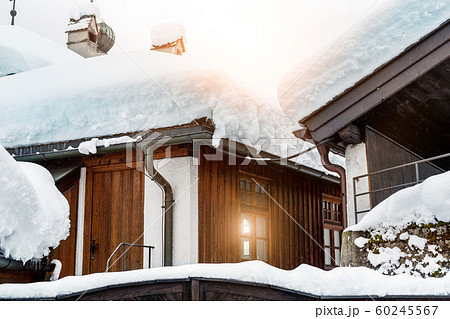 Roof of ancient wooden building covered with thick snow drift layer after heavy snowfall blizzard on street old european austrian Kufstein town. Scenic winter weather background. sun in small window Roof of ancient wooden building covered with thick snow drift layer after heavy snowfall blizzard on street old european austrian Kufstein town. Scenic winter weather background. sun in small window 60245567