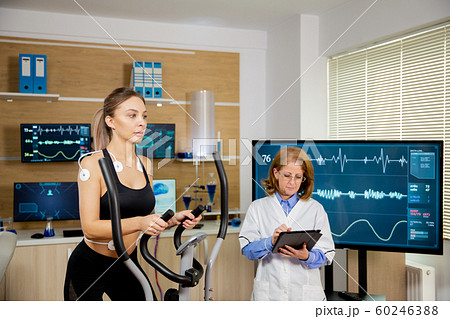 Female athlete testing the stepper with electrodes on her and the doctor making notes in the tablet 60246388