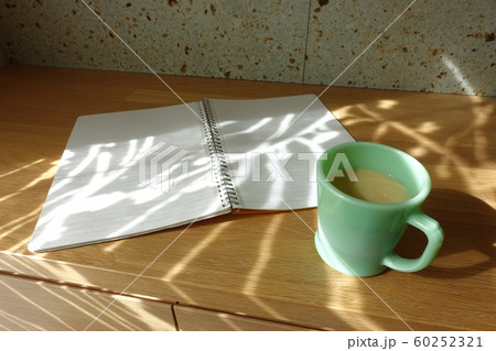 コーヒーカップと白紙のノート　カーテン越しの光が射すテーブルで　cup and notebook 60252321