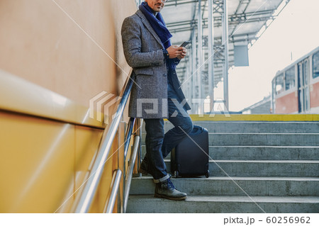 Elegant young man standing on steps and using cellphone Elegant young man standing on steps and using cellphone 60256962