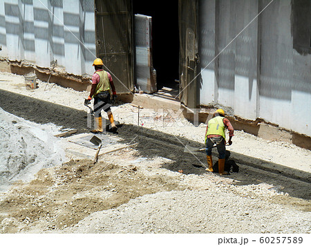 Construction workers creating concrete road curb at the construction site. They are using the in-situ method using the standard metal mold.  60257589