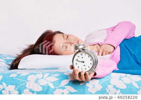 Young woman fallen asleep with alarm clock in hand 60258220