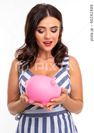 European attractive brunette in dress holds a piggy bank in her hands on a white studio background 60262889