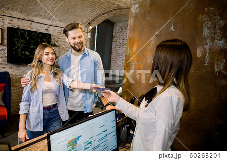 Happy smiling couple giving their reservation details and passports to a concierge while checking in together at the reception counter of a hotel Happy smiling couple giving their reservation details and passports to a concierge while checking in together at the reception counter of a hotel 60263204