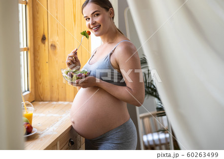 Happy pretty pregnant female standing near window 60263499