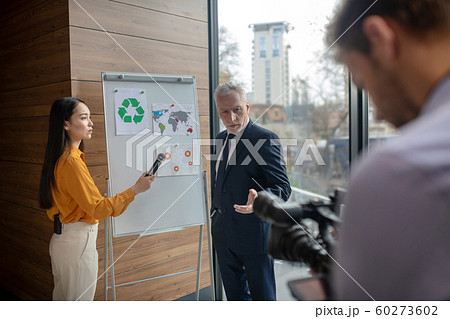 Dark-haired female reporter standing near the white board 60273602