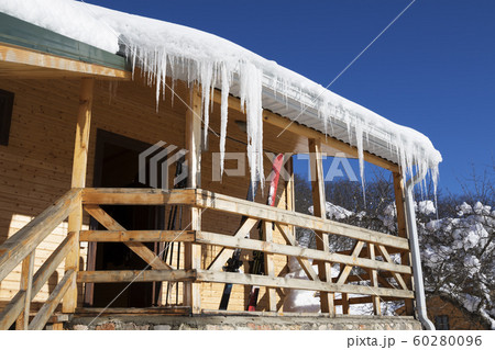 Wooden house with big icicles on roof and ski 60280096