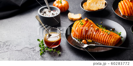 Roasted pumpkin with honey sauce and herbs on a black plate. Slate background. Copy space. 60283772