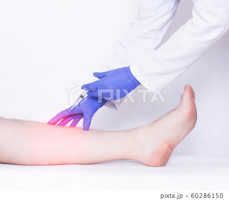The doctor makes an injection into the calf muscle to the patient of an anti-inflammatory drug to relieve pain and inflammation, stretching the ligament on the leg The doctor makes an injection into the calf muscle to the patient of an anti-inflammatory drug to relieve pain and inflammation, stretching the ligament on the leg 60286150