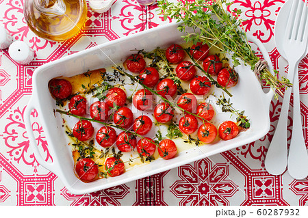 Roasted cherry tomatoes with fresh herbs in baking dish. Mediterranean colorful print background. Top view. 60287932