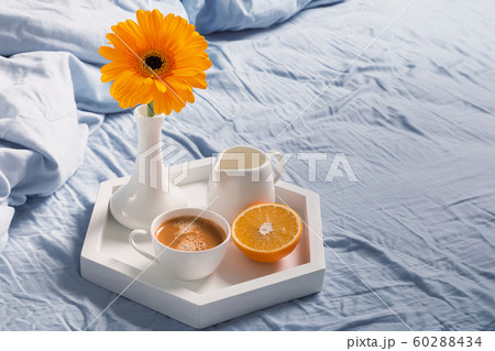 Tray with coffee, milk, orange and yellow flower in a vase on it standing on the bed. 60288434