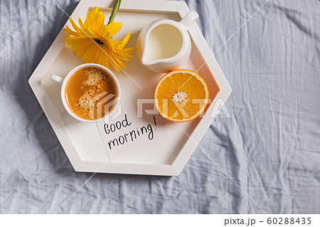 Tray with coffee, milk, orange and yellow flower on it standing on the bed 60288435