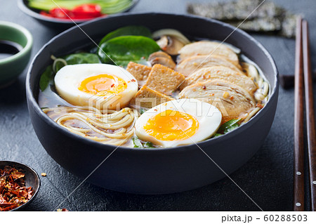 Asian noodle soup, ramen with chicken, tofu, vegetables and egg in black bowl. Slate background. Close up. 60288503