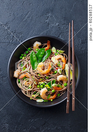 Stir fry noodles with vegetables and shrimps in black bowl. Slate background. Top view. 60288517