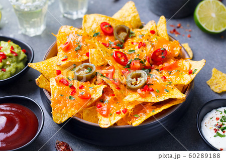 Nachos chips with melted cheese and dips variety in black bowl. Grey stone background. 60289188