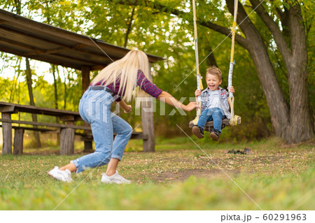 Young blonde mom shakes her little son on a swing 60291963