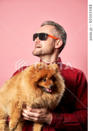 Happy male in sunglasses with spitz in his hands on empty pink background Happy male in sunglasses with spitz in his hands on empty pink background 60303488