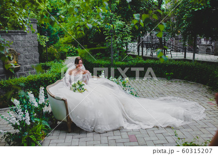 Young beautiful bride in luxury dress with a long train sitting on a sofa 60315207